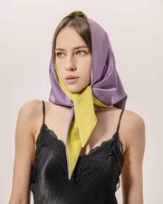 Woman wearing a purple and olive color scarf on a plain background
