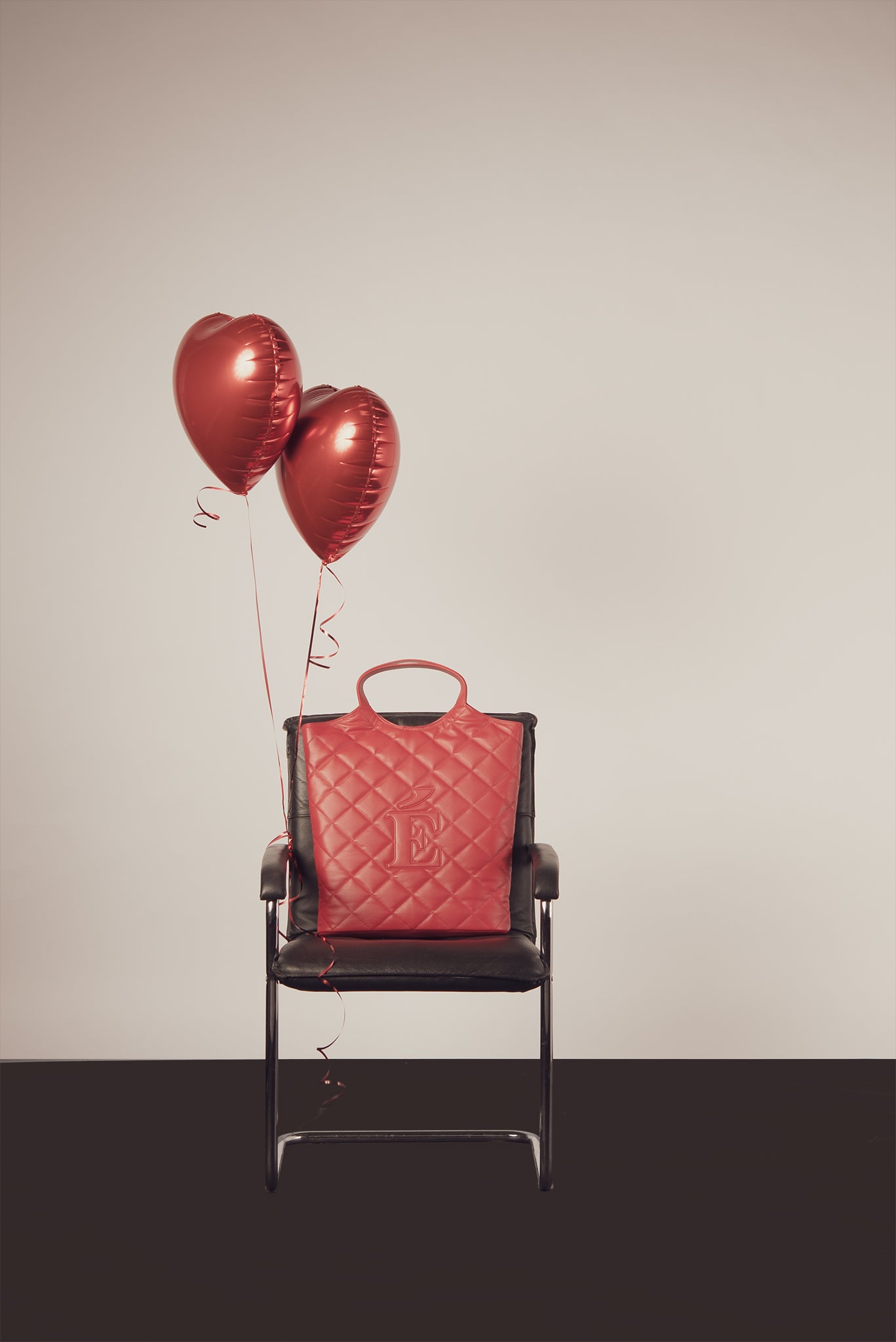 Anna red quilted bag by even-online on a chair with two heart-shaped balloons against a beige background