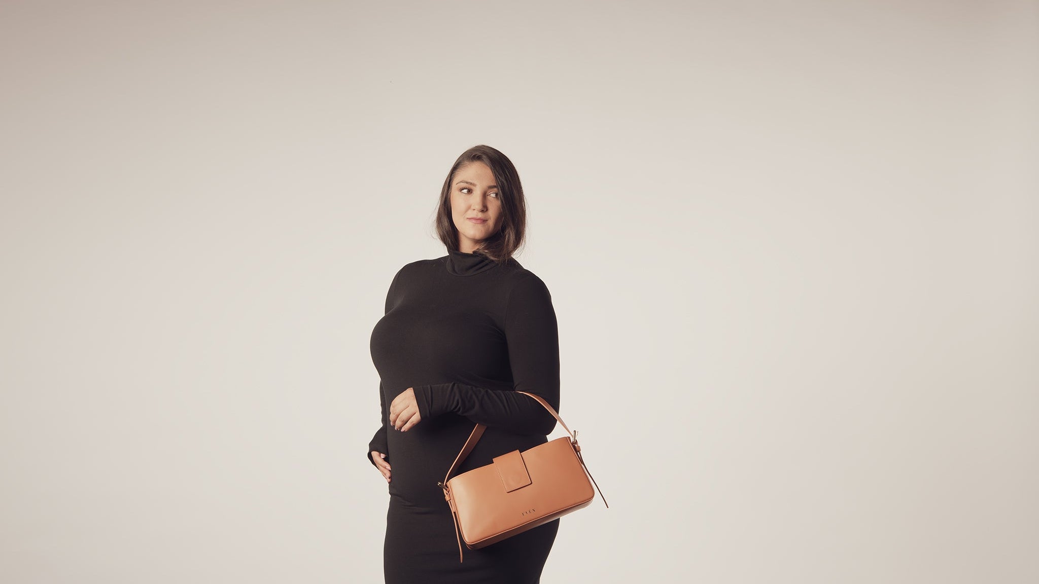 Woman holding a cognac color leather handbag against a plain background