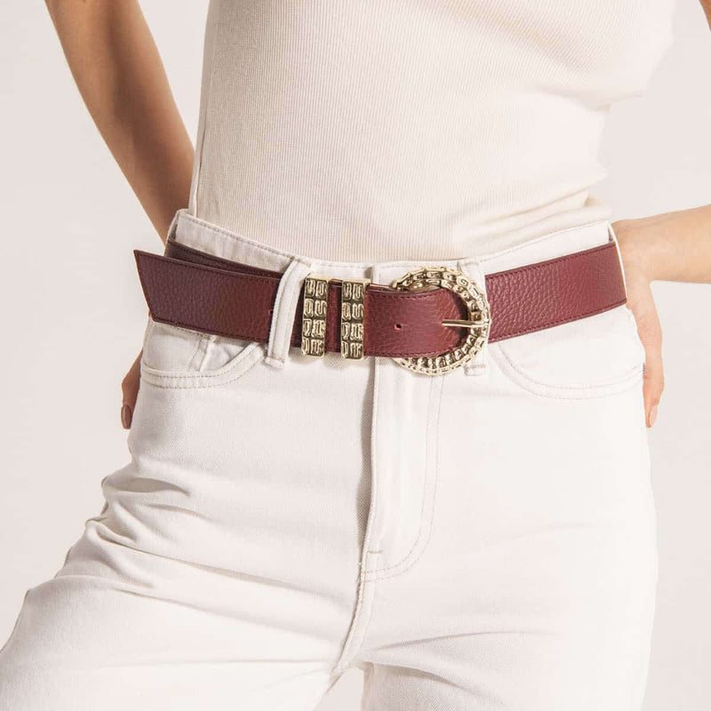 Maroon belt with decorative buckle worn by a person on a white background