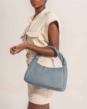 Woman showing Monna mini tote bag in light blue leather with gold tone logo by even-online.