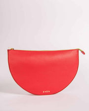 Red half-moon Leyza clutch with gold zipper on a light pink background