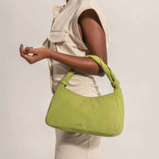 Person holding a green handbag with a plain background with gold even logo