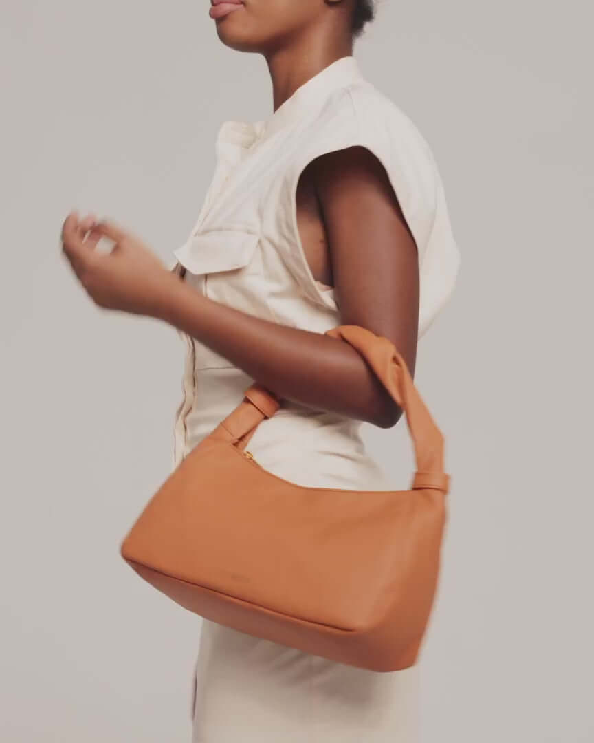 Model showing Monna mini tote bag in cognac color leather styled with natural color top