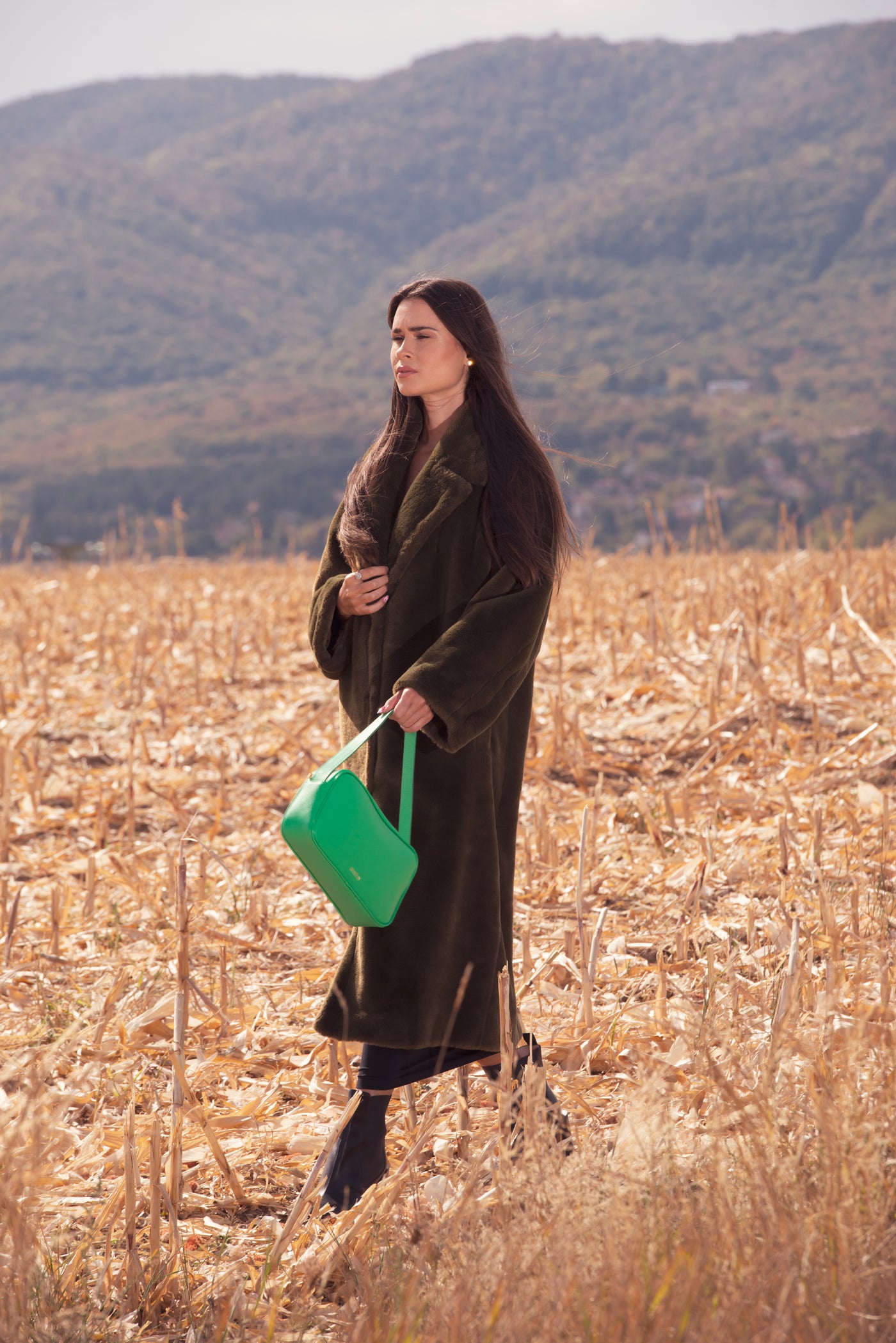 Woman holding a green bag in a field with mountains in the background