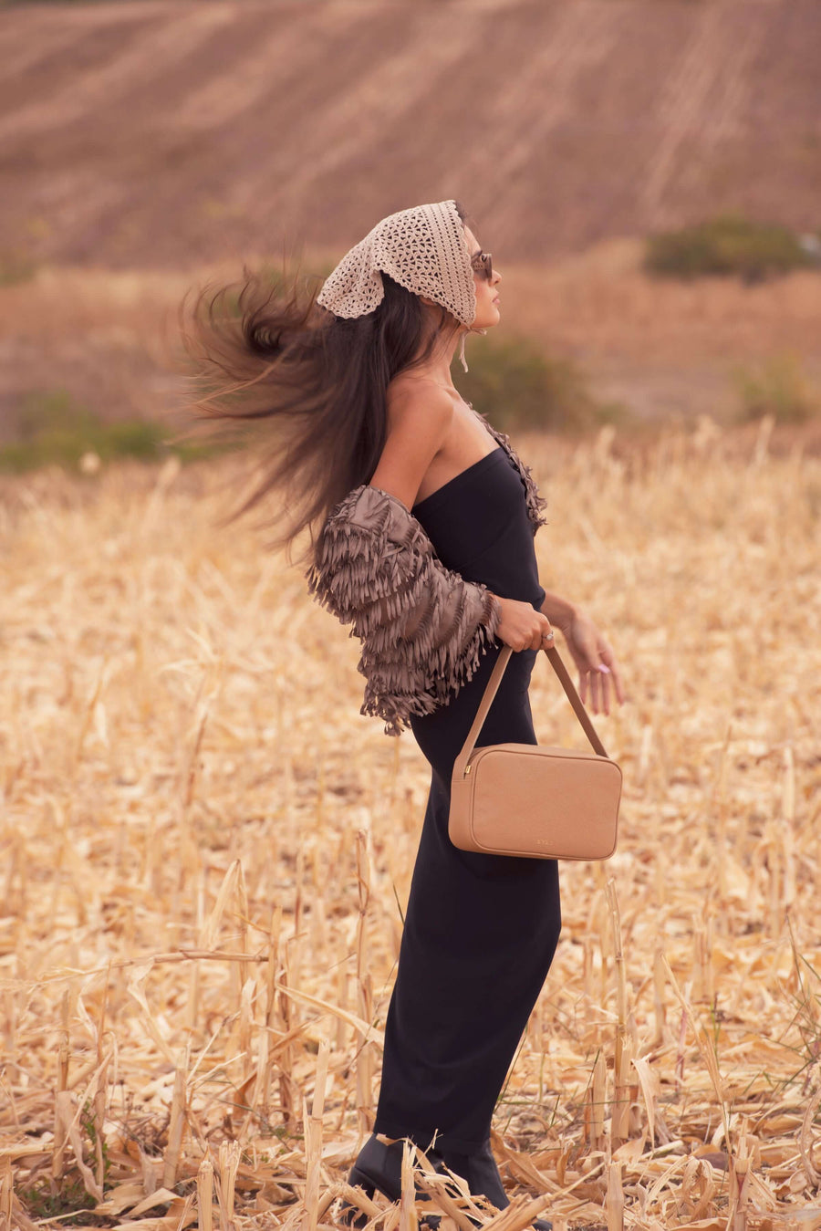 Woman in a black outfit with a beige handbag standing in a field