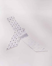 A white satin Jana hair bow with a logo print, positioned diagonally against a white background.