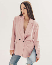 Woman in pink blazer holding Leyza clutch in blue leather.