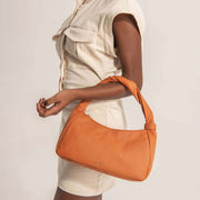 Model wearing orange leather shoulder bag with adjustable strap styled with cream blazer